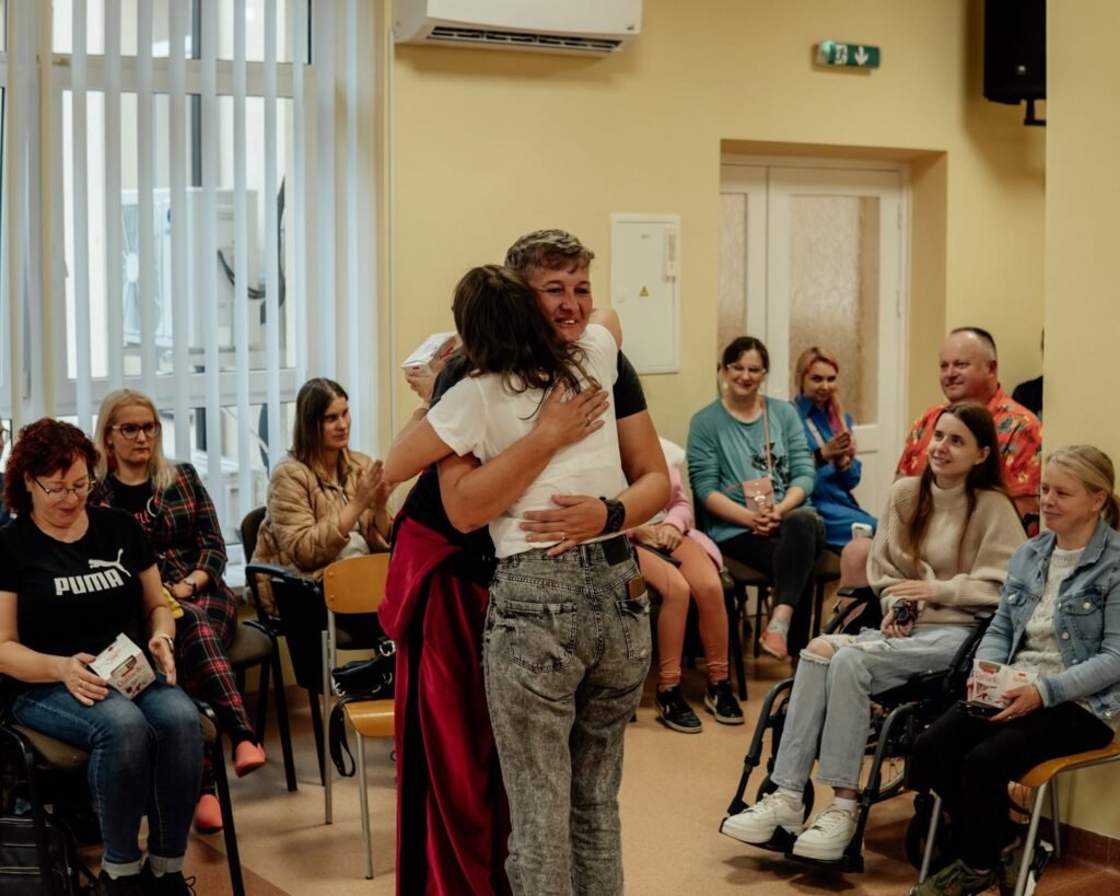 Du žmonės apsikabina renginio metu, aplinkiniai ploja