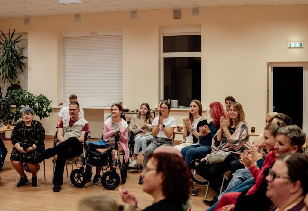 Salė su susirinkusiais dalyviais, kurie ploja