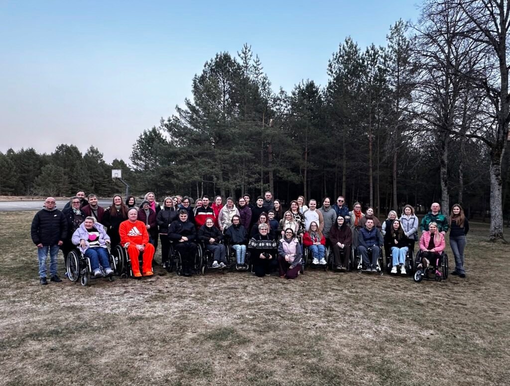 Bendruomenės narių grupinė nuotrauka lauke prie miško
